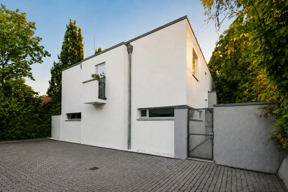 Wohnhaus mit weißer Fassade, Eingangstor und umgebenden Bäumen